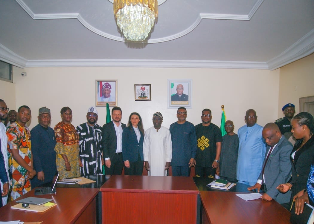 Group of officials and dignitaries standing around a conference table in a formal government office with portraits on the wall and Nigerian flag visible